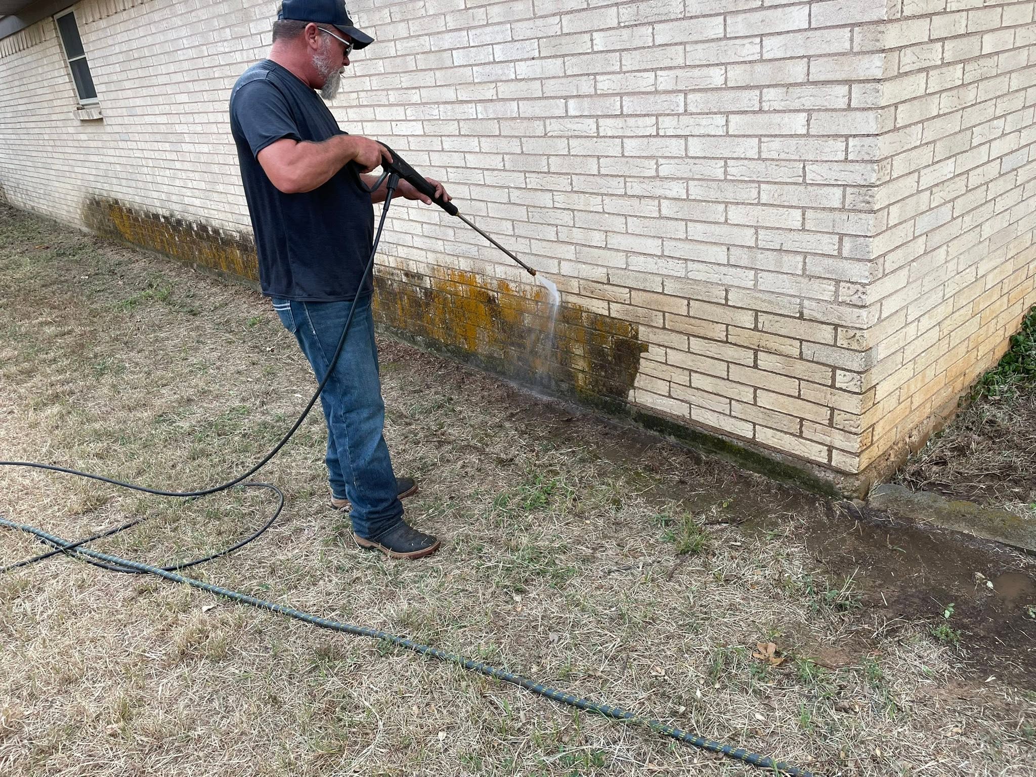 Pressure washing a brick exterior wall in progress
